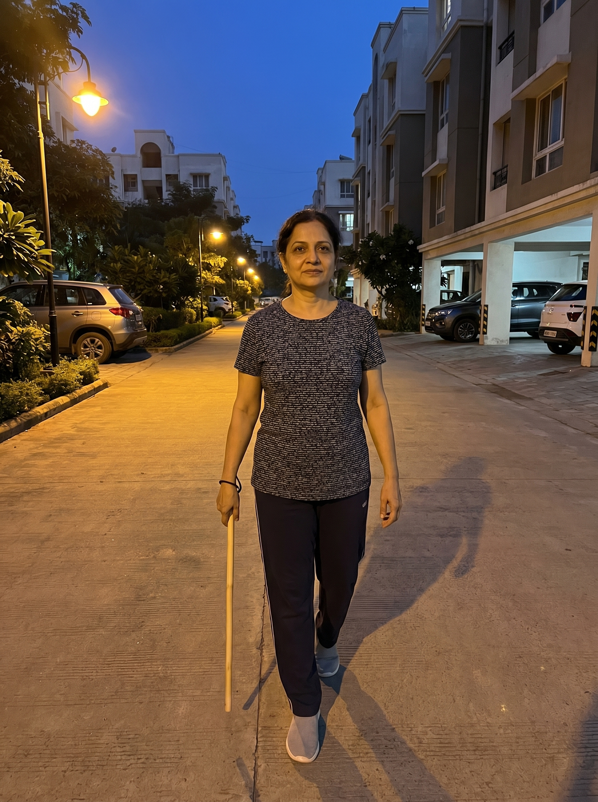 Woman walking an evening residential-society lane carrying the natural Bamboo Safety Stick in hand