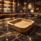 Bamboo square ashtray on a marble countertop with a blurred bar background