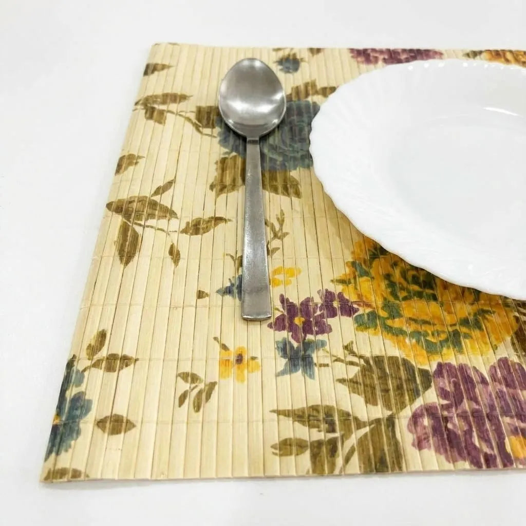 Floral-patterned bamboo placemat with a white plate and silver spoon on a white background