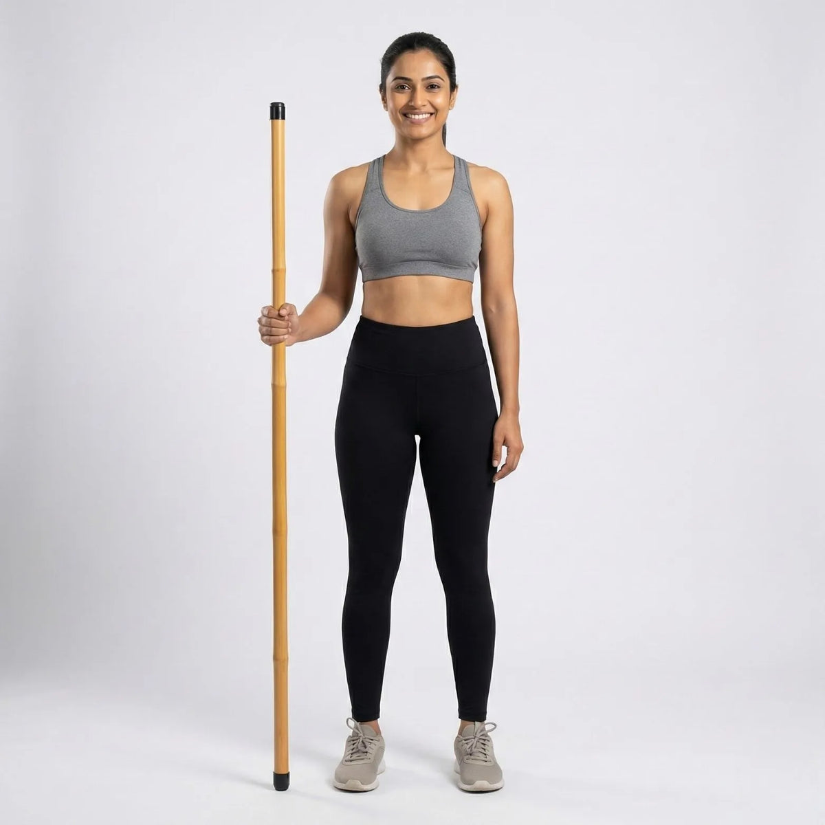 A woman standing with a Bamboo Yoga Stick, promoting posture and flexibility in workout attire.