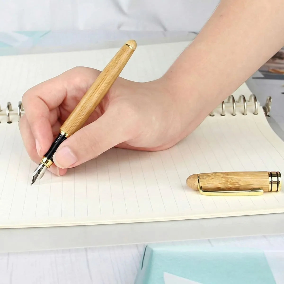 Hand holding a Premium Bamboo Pen, writing in a notebook, showcasing its comfortable grip and design.