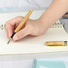 Hand holding a Premium Bamboo Pen, writing in a notebook, showcasing its comfortable grip and design.