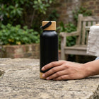 Hand resting beside the Bamboo Steel Water Bottle on a stone garden bench