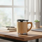 Bamboo Travel Coffee Mug on a wooden table near a window with a plant in the background.
