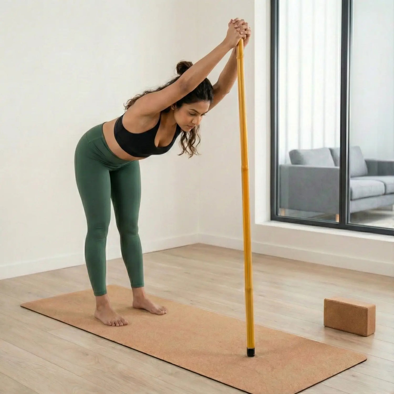 Woman practicing yoga with a bamboo fitness stick in a modern living room.