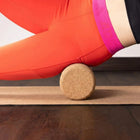 Close-up of a Cork Muscle Roller being used on a yoga mat by a person in bright workout leggings.