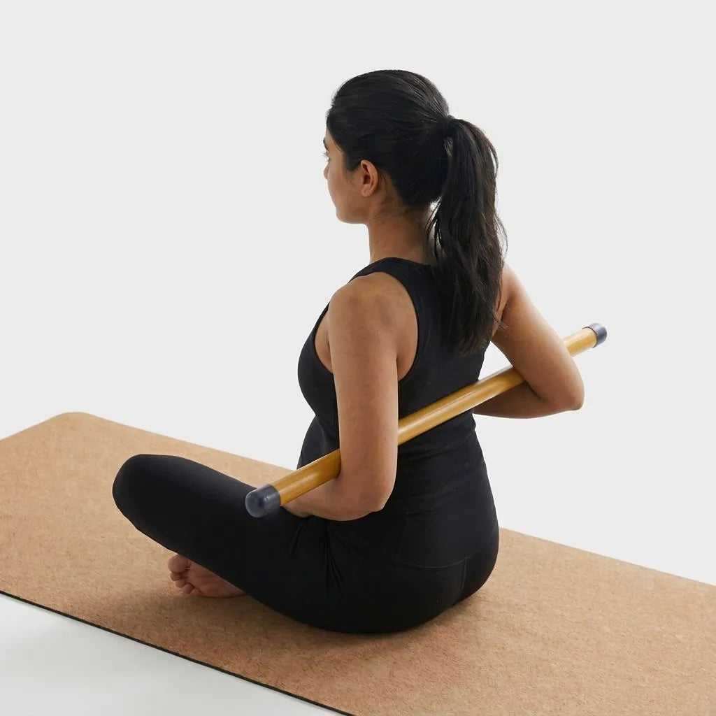 Woman sitting on a cork mat with a bamboo yoga mini stick, wearing a black outfit.